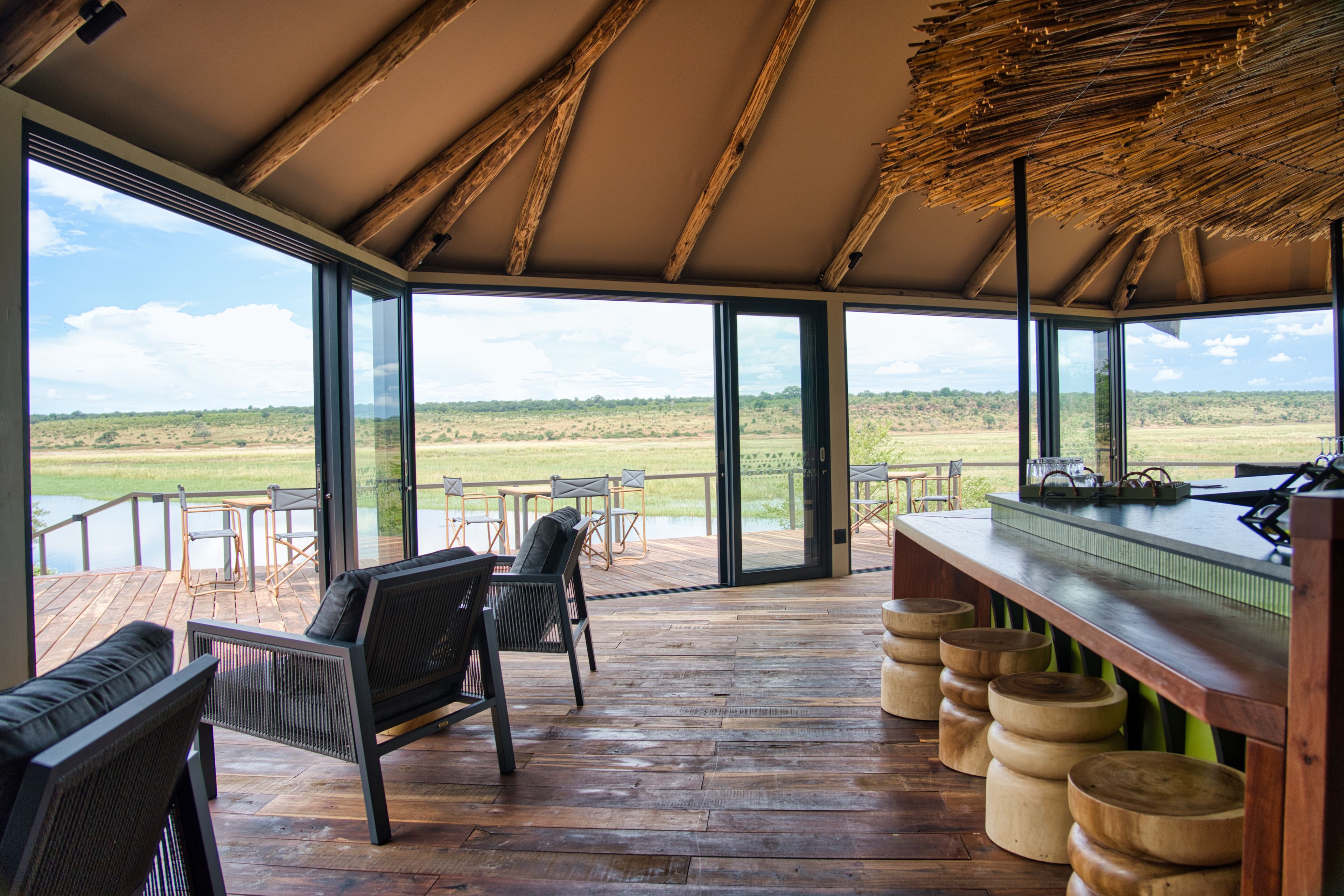 Eine geräumige Veranda mit Holzboden, einer Bar mit Hockern und großen Glasüren, die zu einem Außenbereich führen.