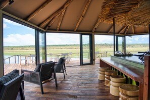 A spacious veranda with wooden flooring, a bar area with stools, and large glass doors leading to an outdoor view.