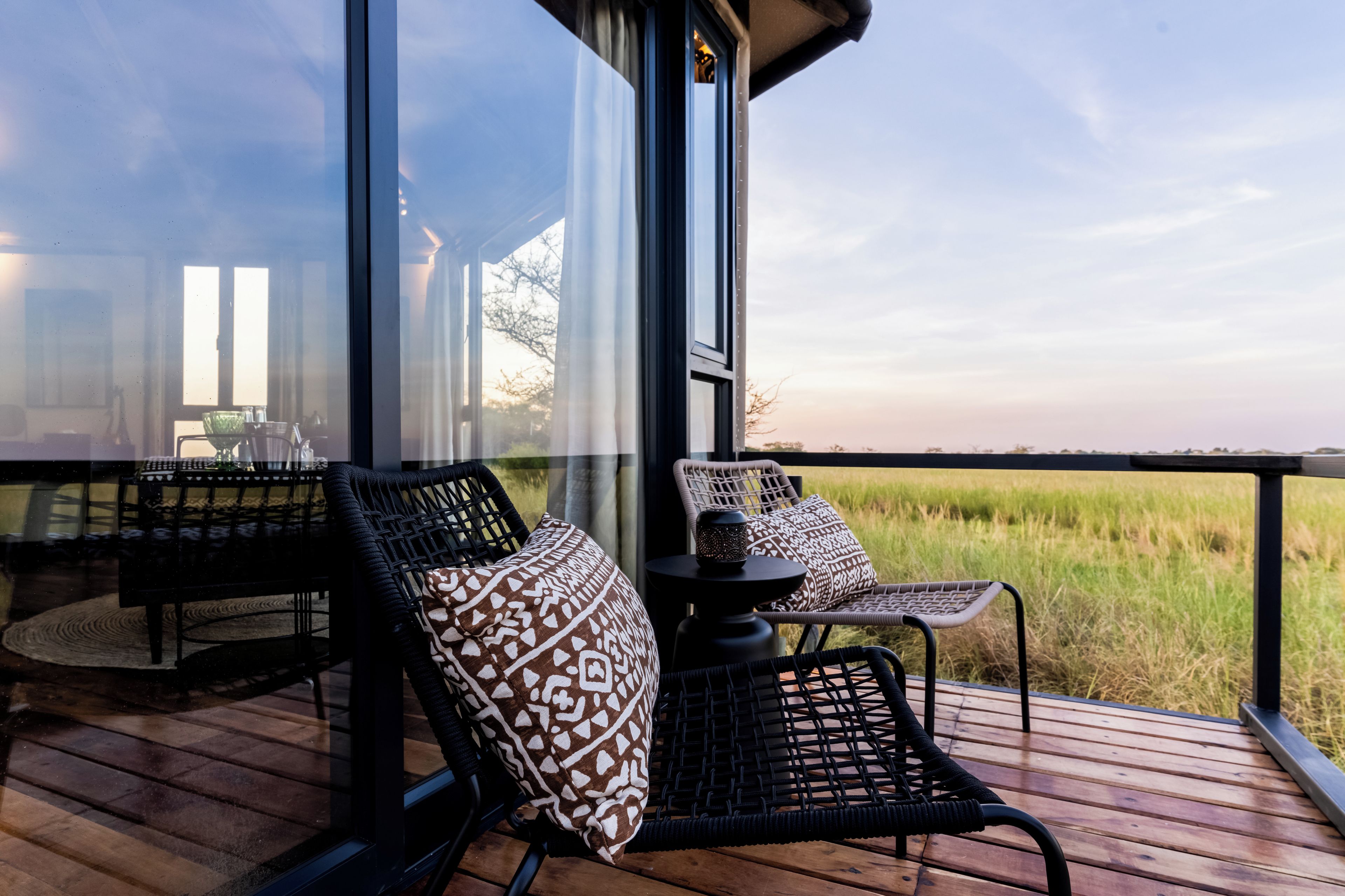 A deck with wicker chairs and a table, overlooking a grassy field.