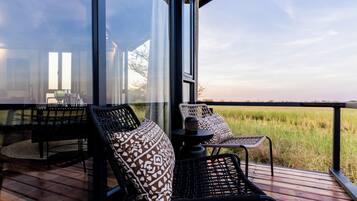 A deck with wicker chairs and a table, overlooking a grassy field.