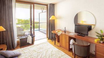 Habitación de hotel con cama, escritorio con televisor, una silla, una mesita y balcón con vista al mar.