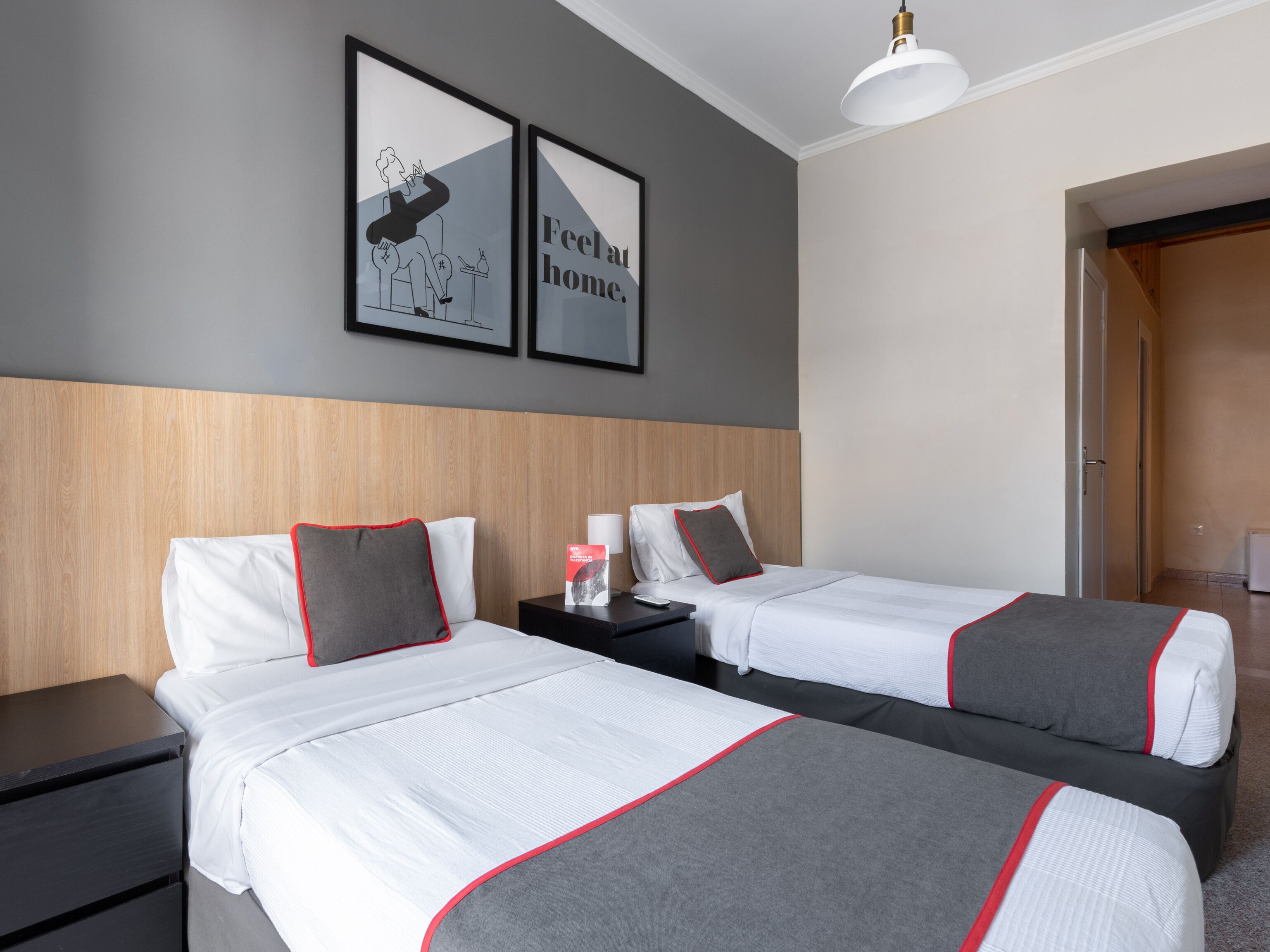 Ein Hotelzimmer mit zwei Betten, einem Holzkopfteil, einem Nachttisch mit Lampe sowie zwei gerahmten Bildern an der Wand.
