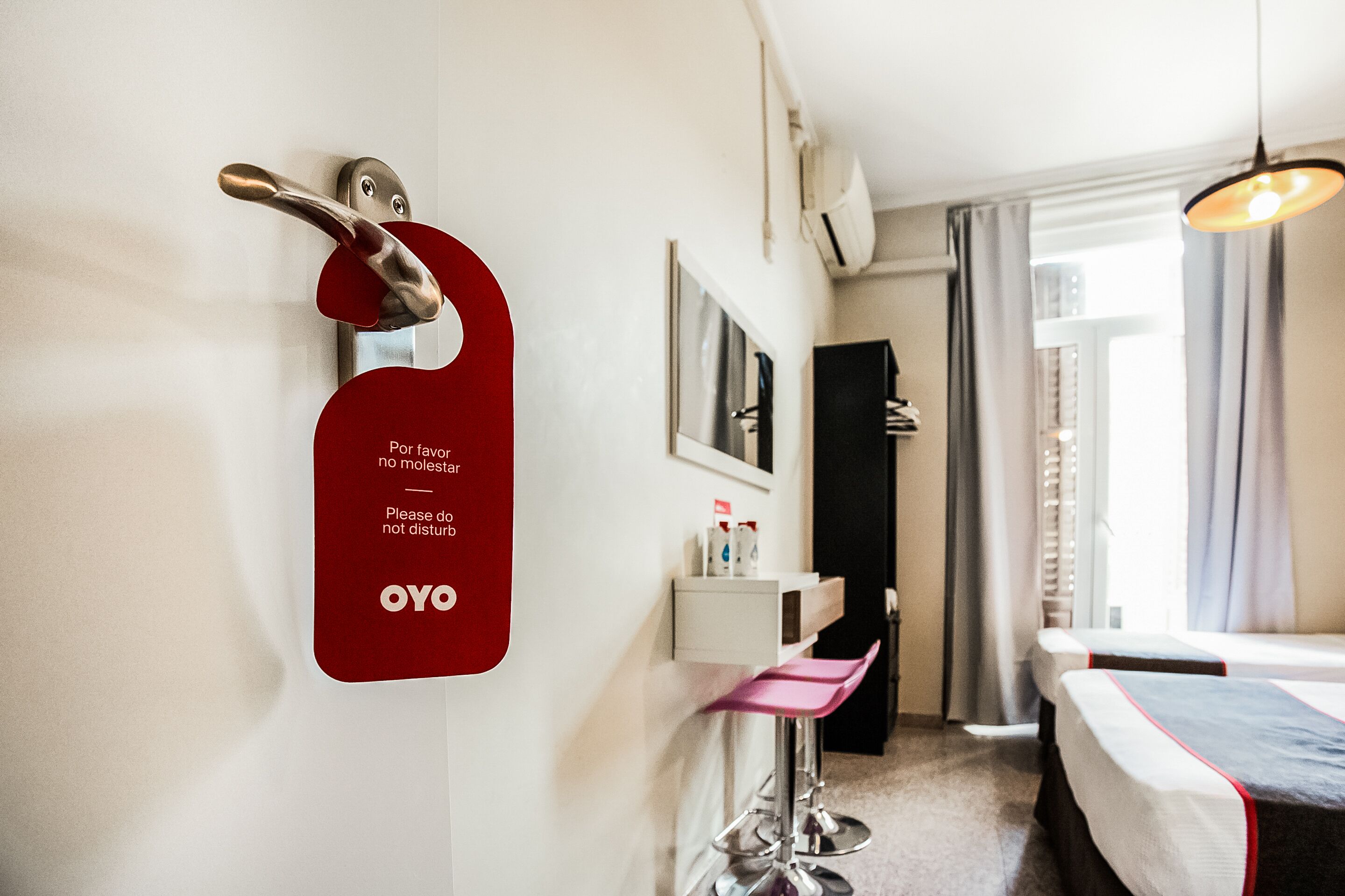 Une chambre d’hôtel avec un lit, un bureau, une chaise, un miroir et une porte avec une pancarte rouge.