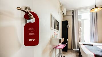 Une chambre d’hôtel avec un lit, un bureau, une chaise, un miroir et une porte avec une pancarte rouge.