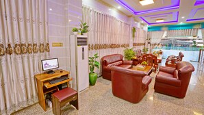 A hotel lobby with a wooden desk, leather sofas, and a computer monitor. - Hotel Shwe Phyo (Mandalay)
