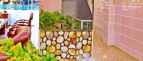 A reception area with a tiled wall featuring a shell pattern, a sign reading "Thanakha Station," and a table with a plant and decorative items.