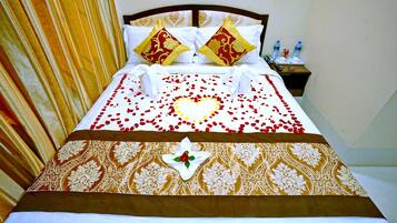 Una cama bien hecha con una decoración en forma de corazón, dos almohadas decorativas y una mesita de noche con botellas de agua.