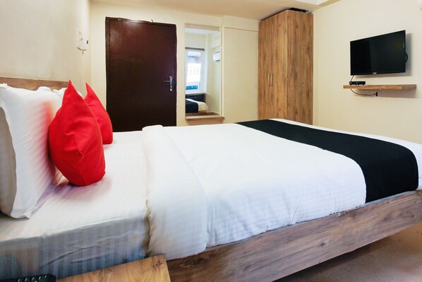 A hotel room with a wooden bed frame, a television mounted on the wall, and a wardrobe. - Royal Derby Suprabhat (Hyderabad)