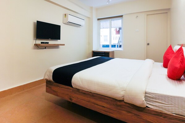 A hotel room with a bed, a TV mounted on the wall, a window with a view, and a door. - Royal Derby Suprabhat (Hyderabad)