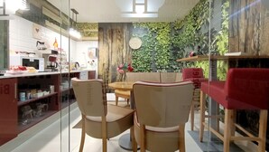 A modern dining area with a wooden table and chairs, a clock on the wall, and a green leafy wall behind the seating. - Hostal Royal Cruz (Madrid)