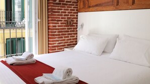 A hotel room with a large bed, a brick accent wall, a wooden headboard, and a cityscape painting. - Hostal Royal Cruz (Madrid)
