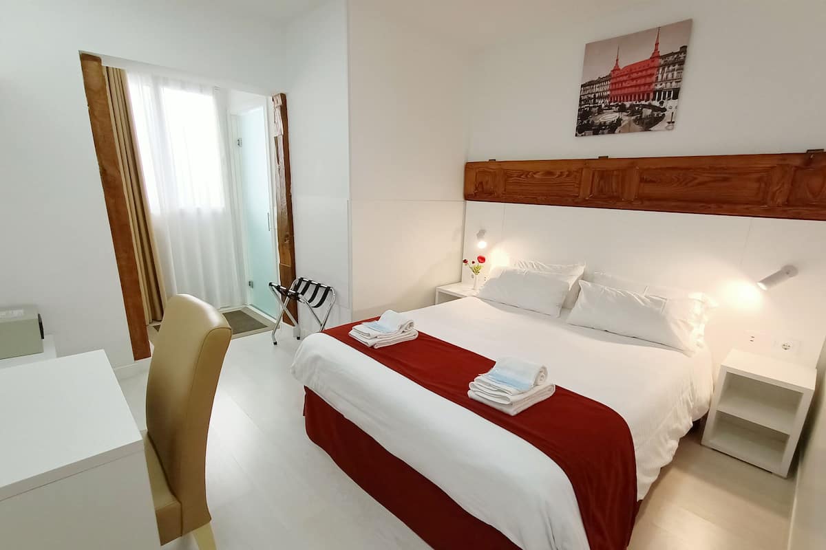 Una habitación de hotel con cama, escritorio, silla y mesita de noche.