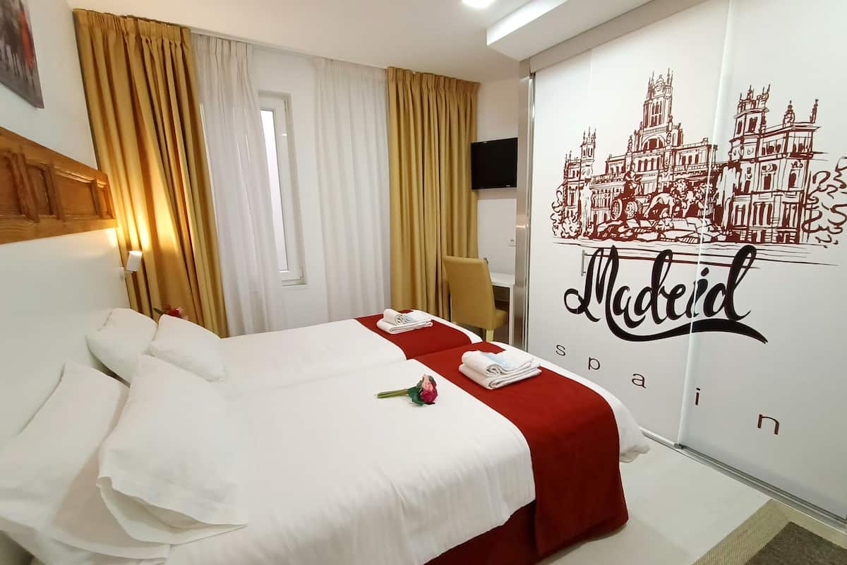 Una habitación de hotel con una cama, una colcha roja y blanca, un ramo de flores y una pared con un mural de la ciudad.
