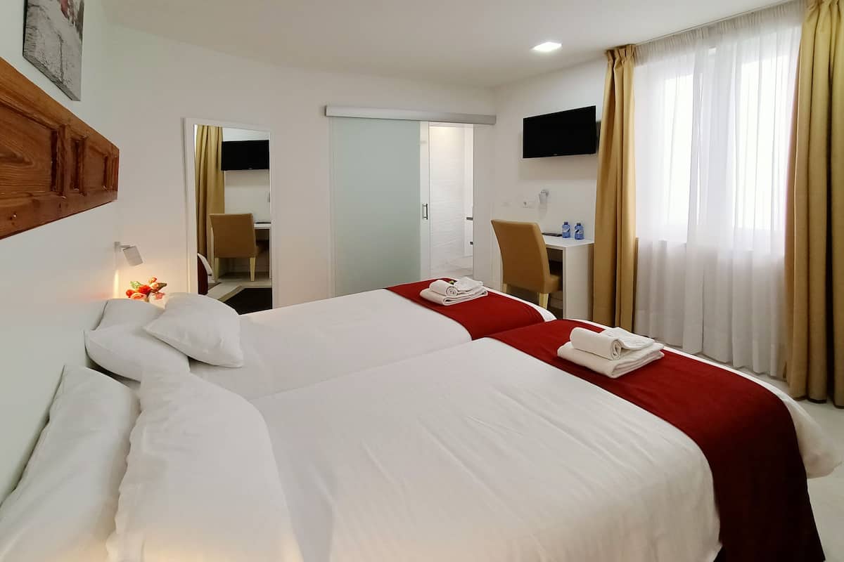 Habitación de hotel con dos camas, un escritorio, una silla, un televisor y un baño visible a través de una puerta abierta.