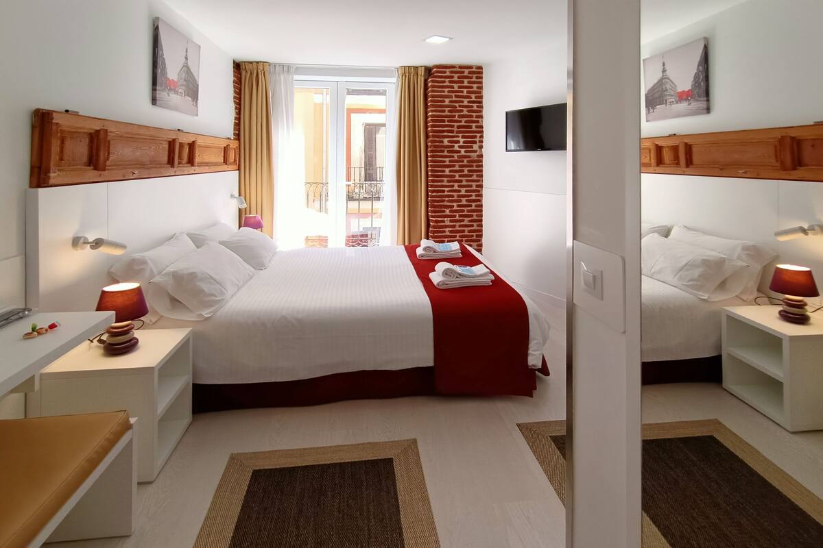 Habitación de hotel con cama, dos mesitas de noche, televisor y vistas al exterior.