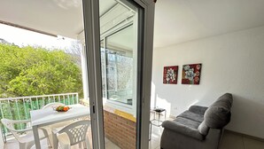 A balcony with a table and chairs, a grey sofa, and two wall-mounted artworks. - Voramar 2A - One Bedroom Apartment, Sleeps 4 (Roses)