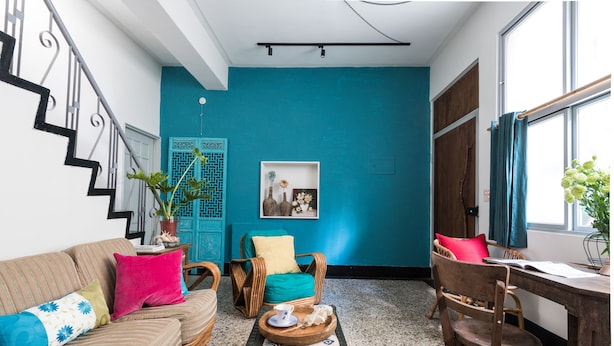Una sala de estar acogedora con una pared de acento color esmeralda, un sofá con cojines de colores, una mesa de centro de madera y un sillón de mimbre.