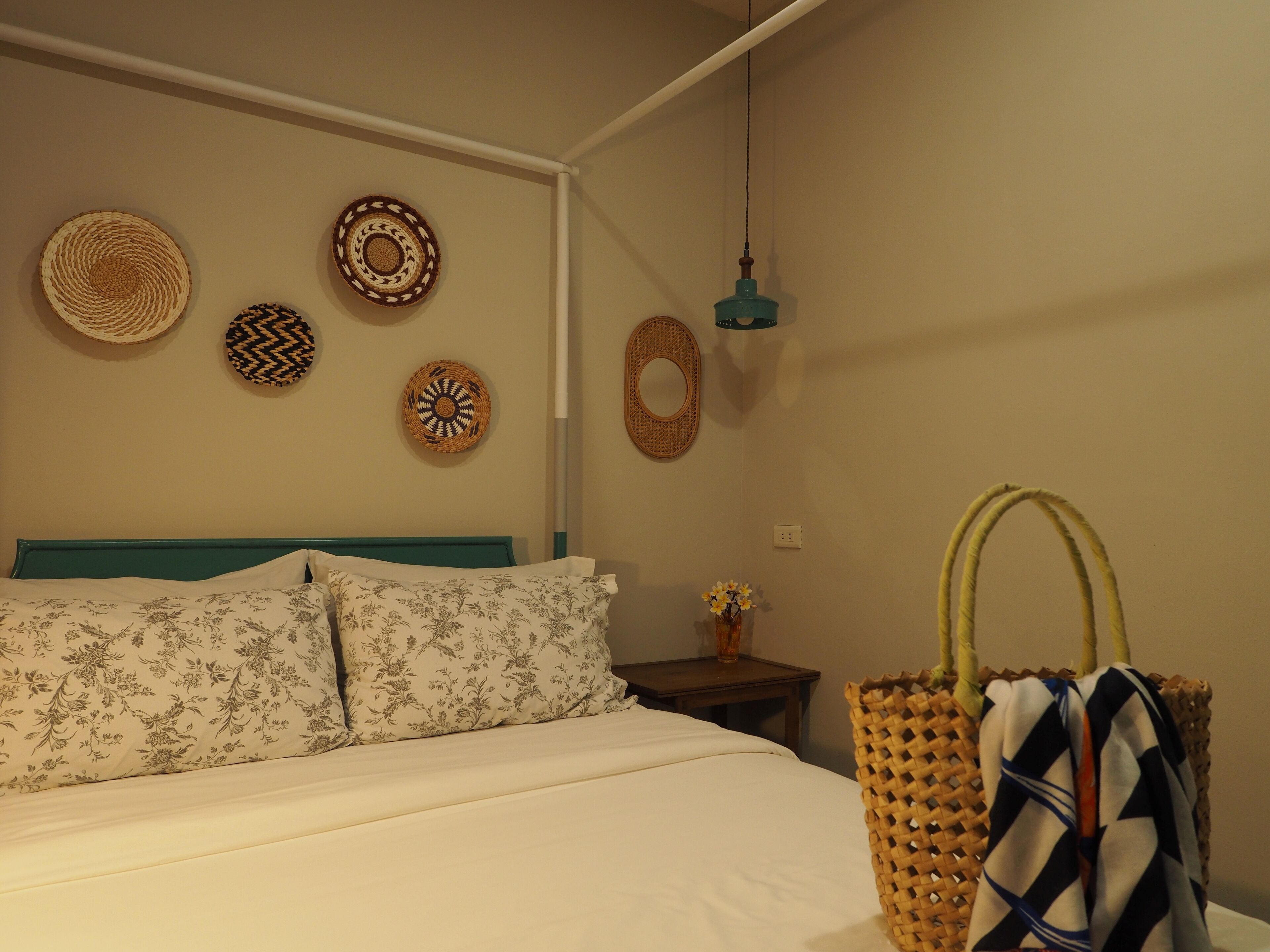 Uma cama bem arrumada com roupa de cama floral, cabeceira verde-água e várias decorações de parede em tear.