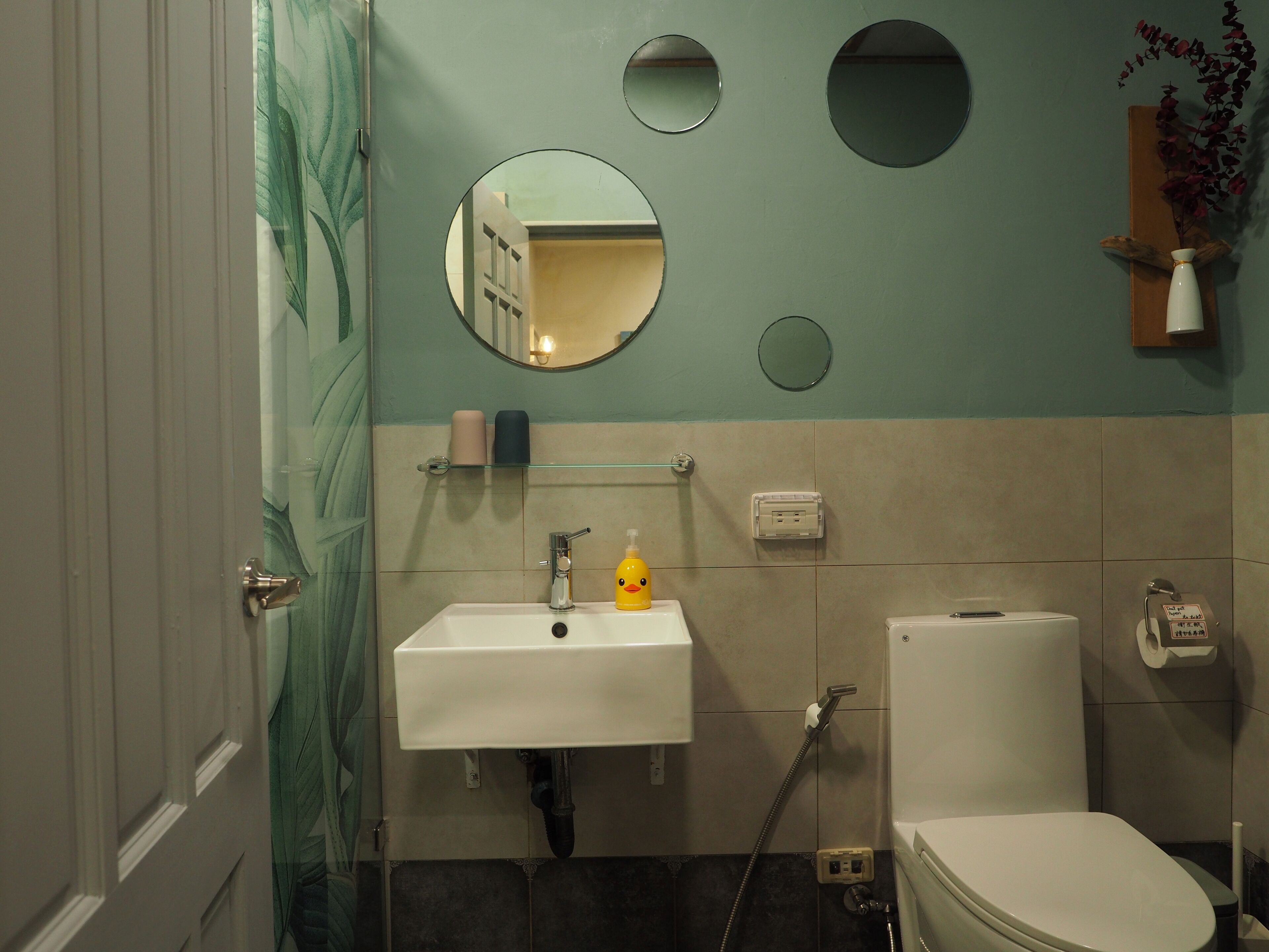 A bathroom with a sink, toilet, and two mirrors. There is a towel rack above the sink and a small shelf with toiletries.