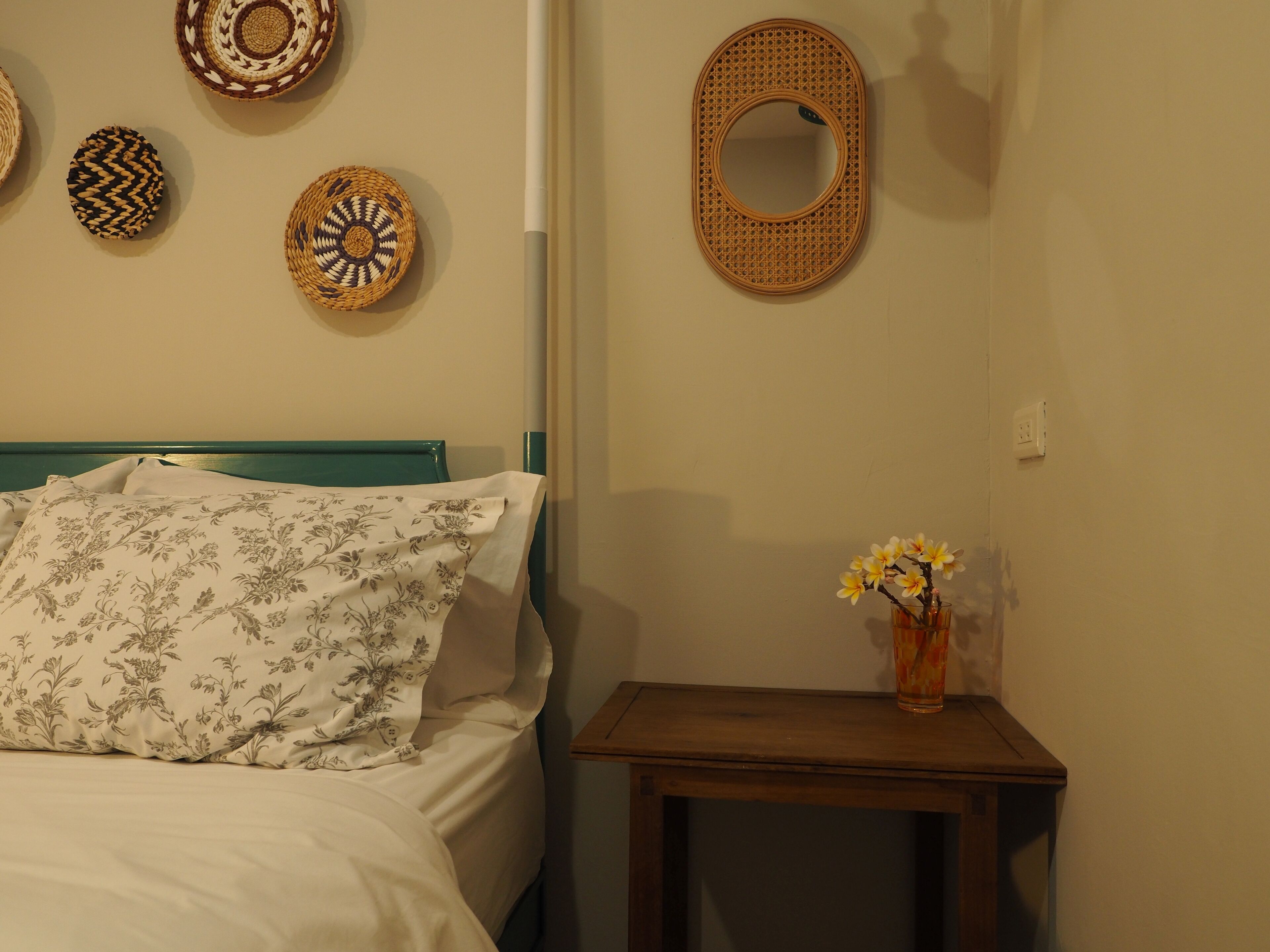 A bed with floral bedding, a bedside table with a vase of flowers, and wall-mounted woven baskets.