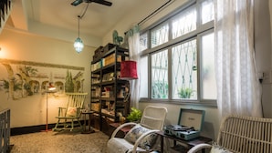 Una sala de estar acogedora con chimenea, una estantería, un sillón mecedor y un ventanal con cortinas.