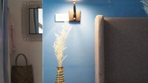 Una habitación con una cama, una lámpara de pared, un florero con flores secas, un espejo y un bolso colgado.