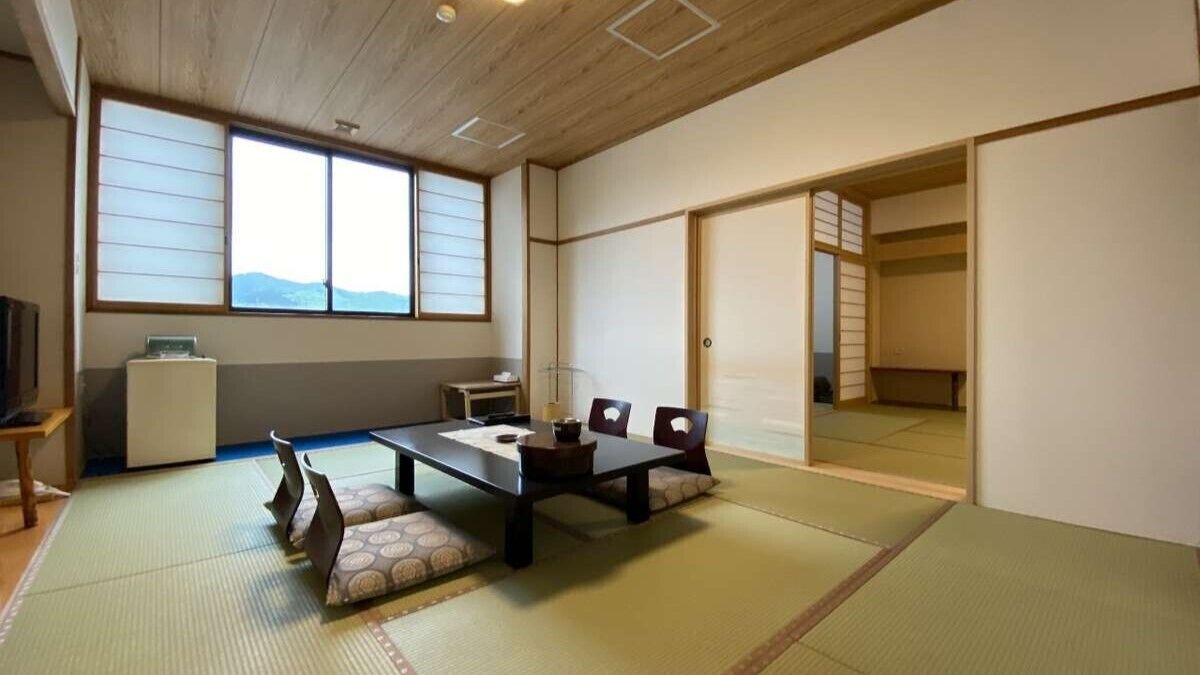 Una habitación japonesa tradicional con suelo de tatami, una mesa baja con cojines, una puerta corredera y vistas al exterior.