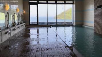 A wet indoor swimming pool with a view of the sea through large windows.
