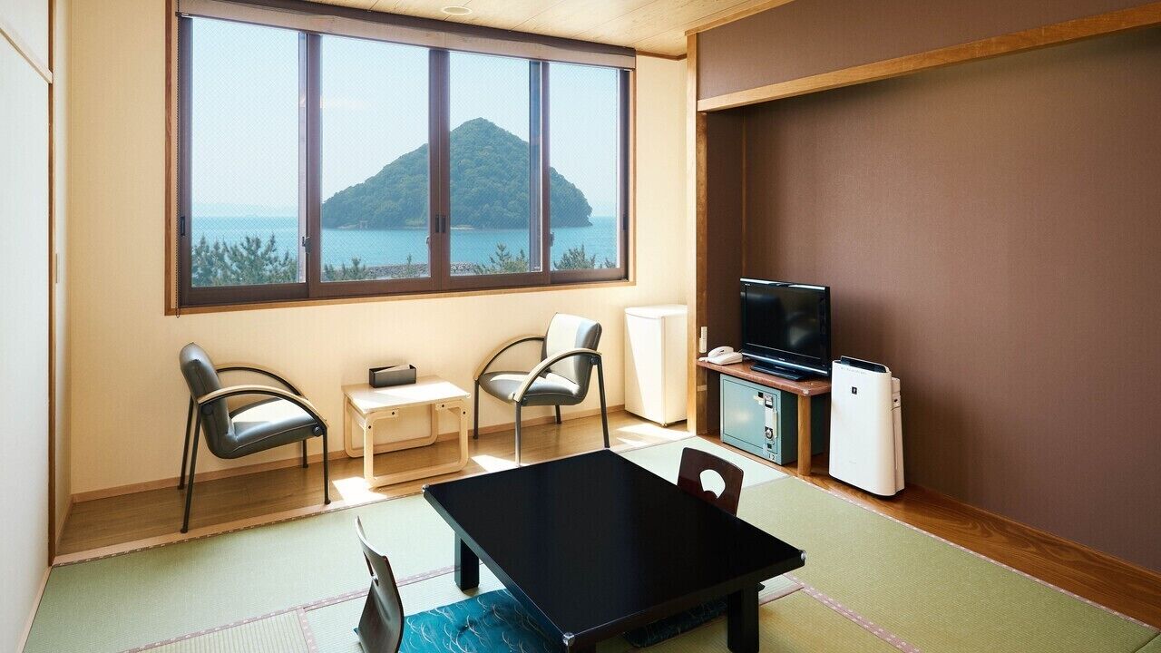 Una habitación con suelo de tatami, una mesa negra, dos sillas, un televisor y un refrigerador.