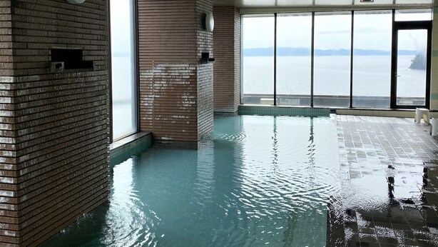 An indoor swimming pool with a view of a body of water through large windows.
