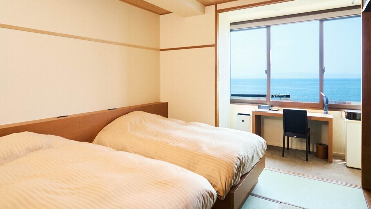 Ein Hotelzimmer mit Bett, Schreibtisch und Blick auf das Meer.