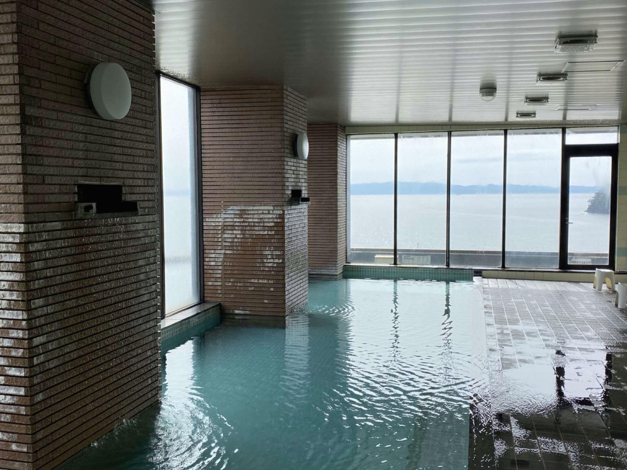 An indoor swimming pool with brick walls and large windows offering a view of the water.