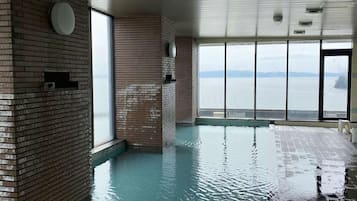An indoor swimming pool with brick walls and large windows offering a view of the water.