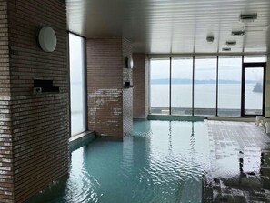 An indoor swimming pool with brick walls and large windows offering a view of the water. - Ryokan Asamushi Onsen Hotel Akitaya (Aomori)