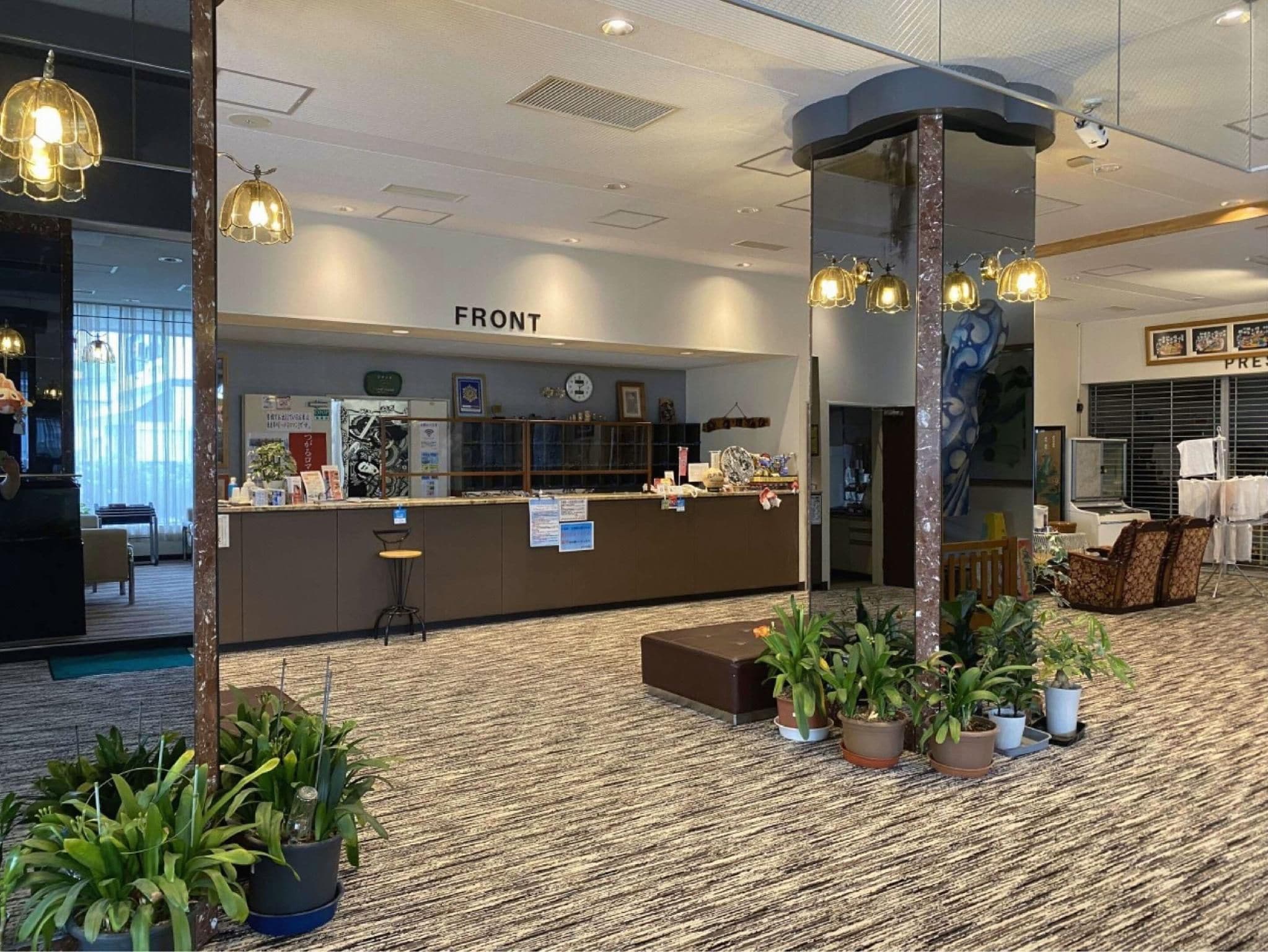 A hotel reception area with a counter, seating, and potted plants.