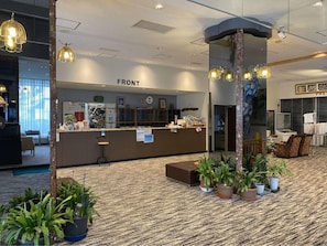 A hotel reception area with a counter, seating, and potted plants.