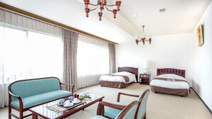 A hotel room with a sofa, two single beds, a table with tea cups, and a chandelier.