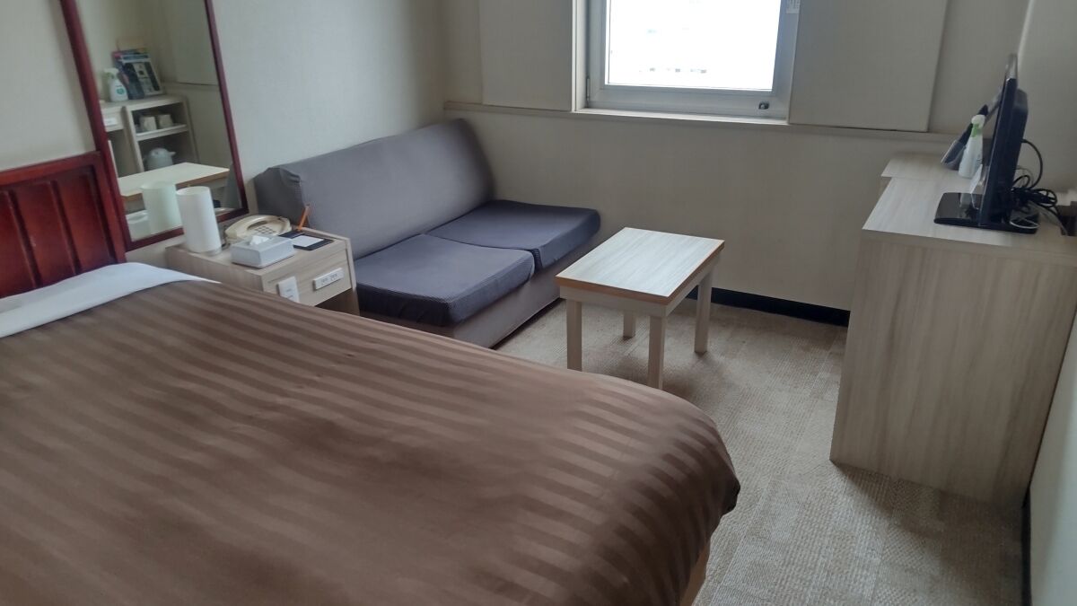 Una habitació d'hotel amb un llit, un sofà, una taula petita, un escriptori, un mirall i una finestra.