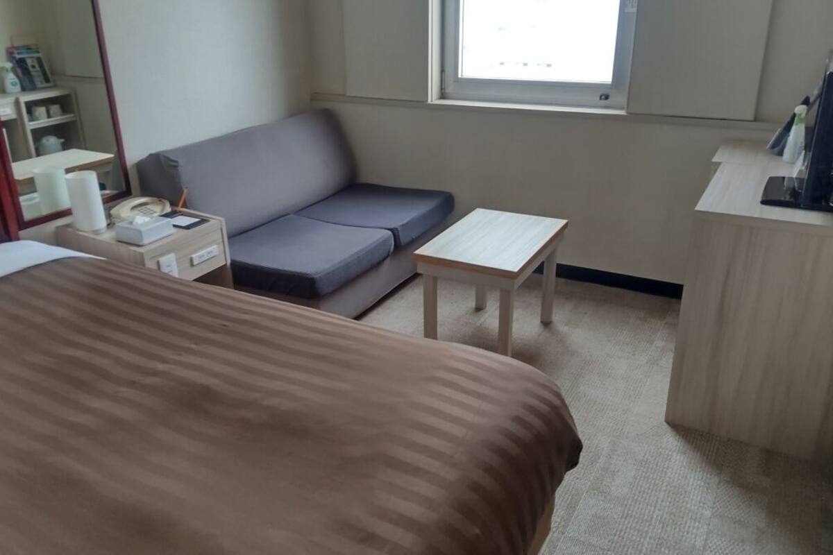 Ein Hotelzimmer mit Bett, Sofa, kleinem Tisch, Schreibtisch, Spiegel und Fenster.