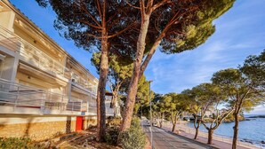 A coastal road with a stone pathway, trees, and a building with balconies overlooking the sea. - Marina 3 - One Bedroom Apartment, Sleeps 4 (Roses)