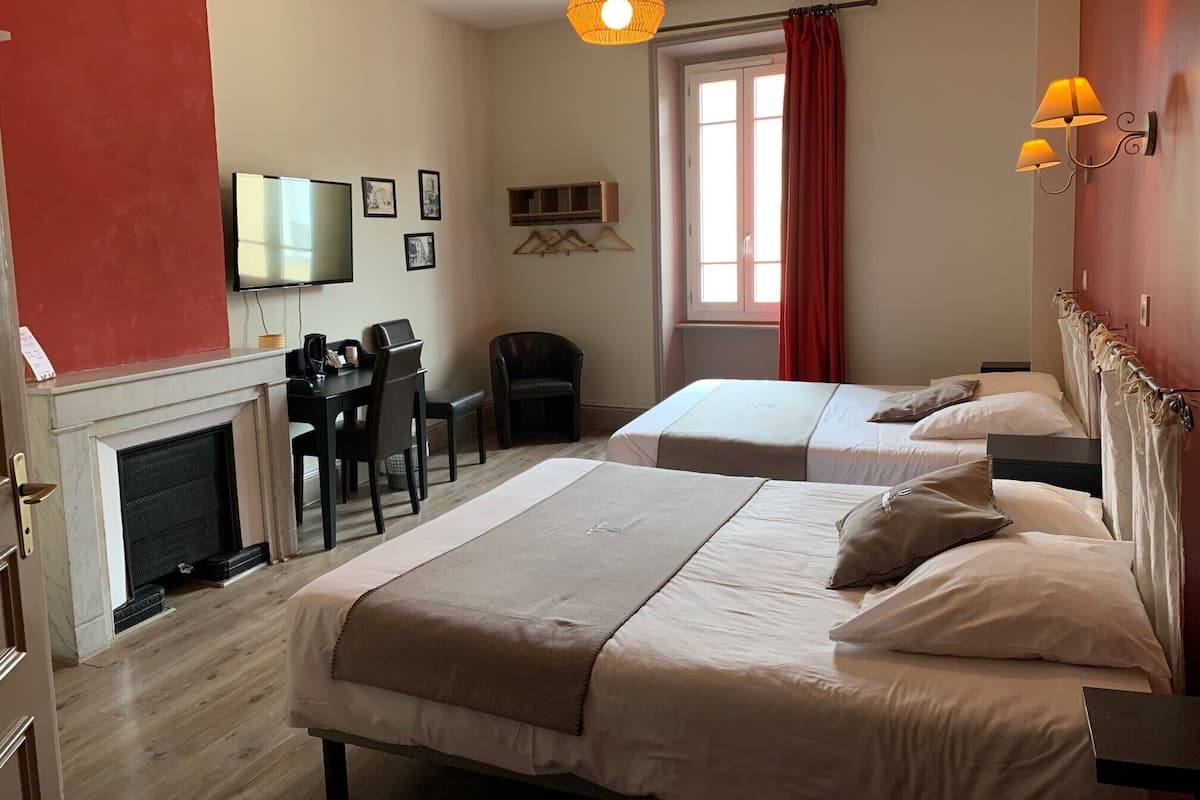 A hotel room with two beds, a desk with a chair, a television, and a fireplace.