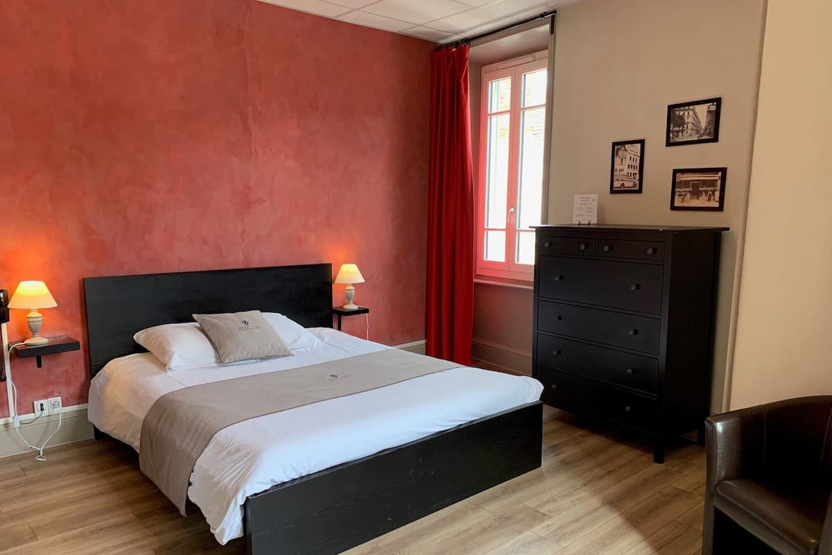 A bedroom with a black bed, two bedside lamps, a dresser, and a chair.