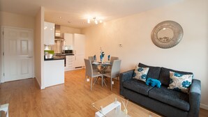 Un salon moderne avec un canapé gris, une table à manger avec des chaises, et une cuisine en arrière-plan.