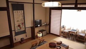 Et traditionelt japansk rum med tatamimåtter, et lavt træbord, et fjernsyn og en skydedør.