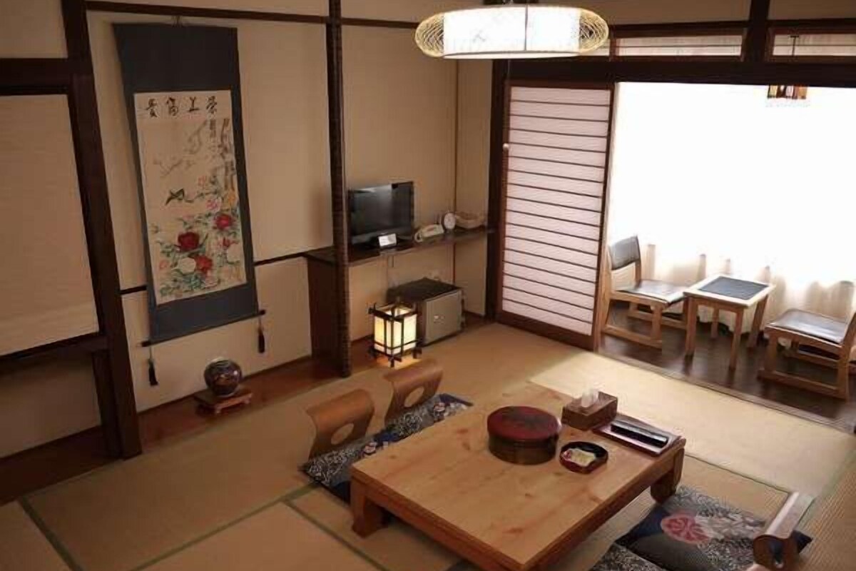 A traditional Japanese room with tatami flooring, a low wooden table, a television, and a sliding door.