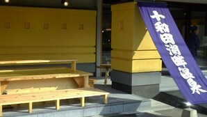 Entrada de un edificio con un banco de madera y un cartel morado con texto blanco.