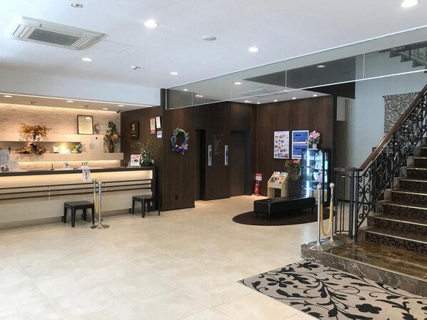 Un vestíbulo de hotel con una recepción, una zona de estar y una escalera.