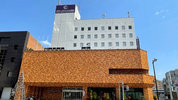 Ett hotell med en modern fasad, en tydlig skylt med texten Hotel Crown Hills Kamashi och en klarblå himmel i bakgrunden.
