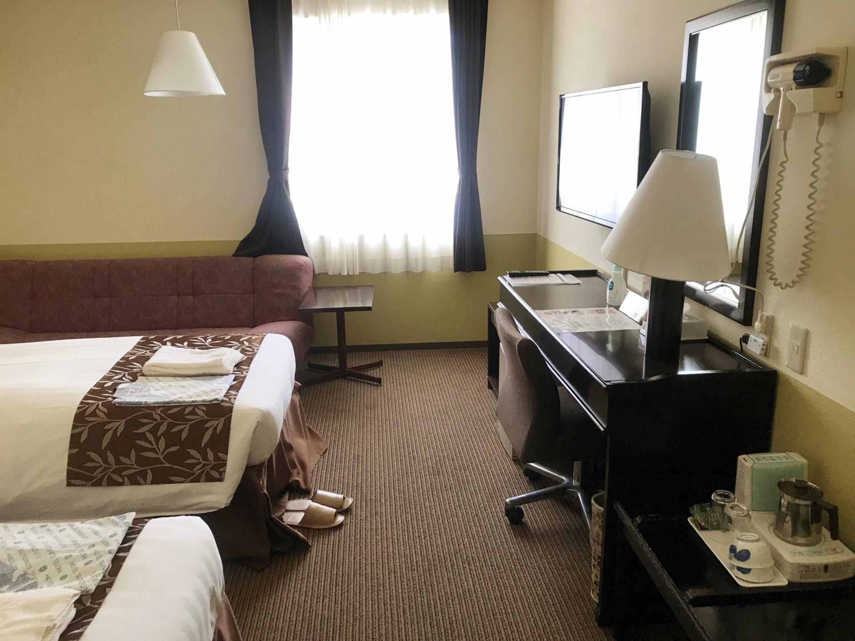 A hotel room with two beds, a desk, a chair, a desk lamp, a telephone, and a window with curtains.