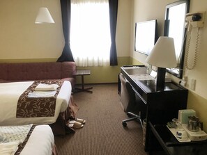 Habitación de hotel con dos camas, un escritorio, una silla, lámpara de escritorio, teléfono y ventana con cortinas.